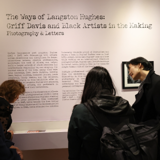 Three people are looking at a wall at the exhibition, The Ways of Langston Hughes. It contains a description of the exhibition. 