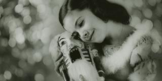 A black and white photo of a girl in a dress hugging a nutcracker in front of a glittering background.