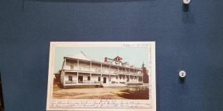 Photograph of a postcard of a house in a display case against a blue background