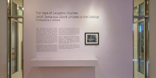 Lavender wall with black text that reads: The Ways of Langston Hughes Griff Davis and Black Artists in the Making Photography and Letters. A framed photo is to the right of exhibition text with a long wall case below.