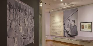 Installation view of floor to ceiling black and white photos of Langston Hughes in a suit surrounded by children and in another image with Hughes standing with a Black man reading Ebony magazine.