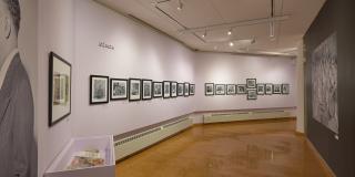 Installation view of lavender gallery walls with black framed b/w photos dotting two walls