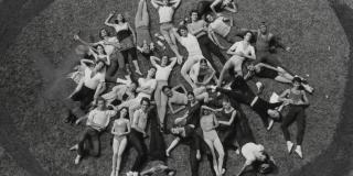 A black and white photo of dancers laying in a group in a field.