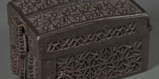 A latched, brown box with slightly curved lid, ornately decorated with carved, interlocking designs