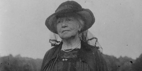 Black and white photo of Lady Gregory standing in a field, wearing all black