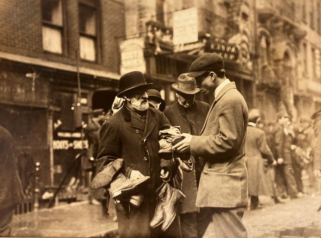 Photograph of shoes-peddler in Lower East Side talking to customers