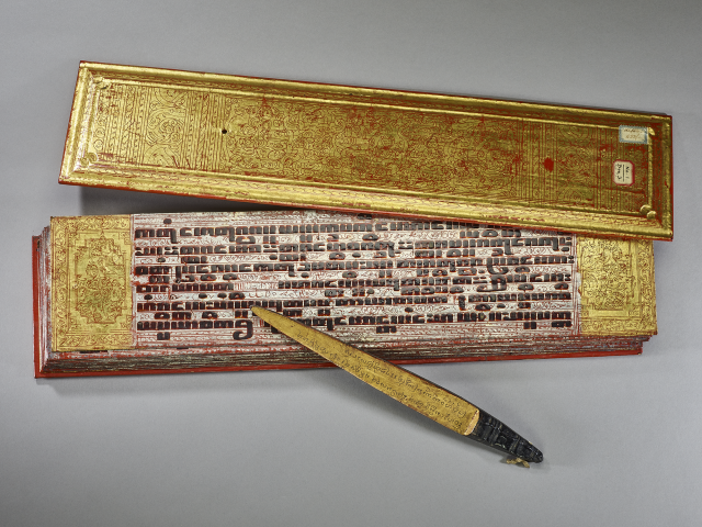 Photo of ornately decorated Buddhist prayer boards painted red and gold with Pāli-language text in black ink. 