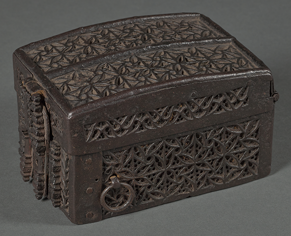 A latched, brown box with slightly curved lid, ornately decorated with carved, interlocking designs