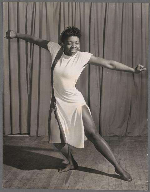 Pearl Primus, is short in a dancing position. One leg is bent holding weight while the other is extended moving in an arc on the wood floor. Both arms are outstretched  away from the body.