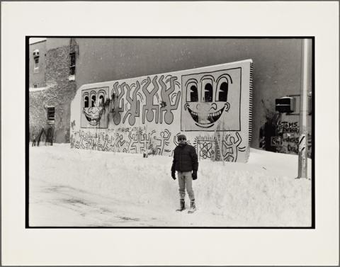 Image of Keith Haring in front of a wall featuring his work.