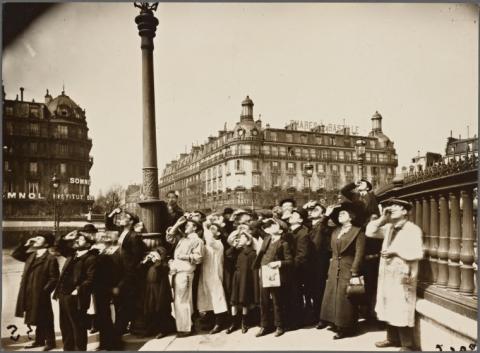 Black and white photo of group of people looking up at sky.