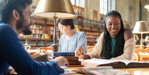 Three researchers sit at a table filled with books in the Rose Main Reading Room. 