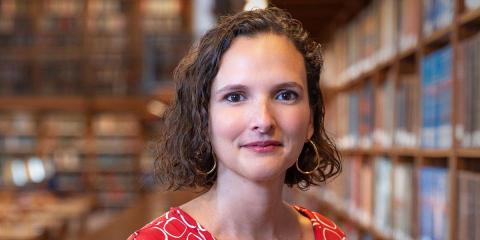 Portrait of Roberta Pereira wearing a red dress with bookshelves in the background.