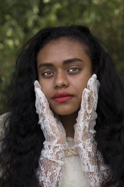 Color portrait of a young woman holding her face between her two hands that are covered with white lace gloves