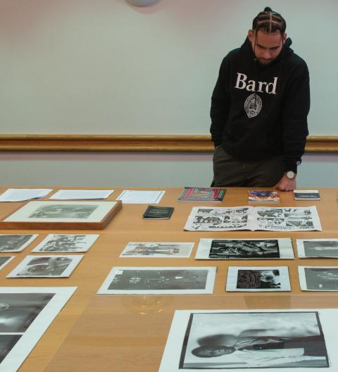 A man standing at a light wood color table with several photographs spread out before him.