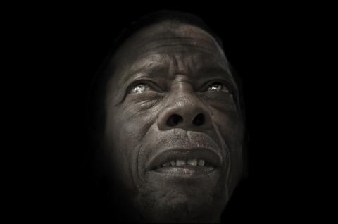 A sepia toned male face partially emerging from a black background.