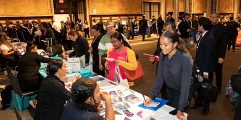 People at a career fair visit various tables with informational flyers.