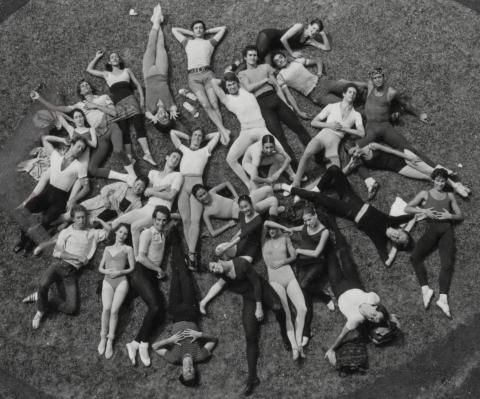 A black and white photo of dancers laying in a group in a field.